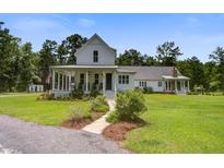 Stunning white farmhouse with a charming front porch and lush, well-maintained landscaping at 105 Bobcat Ln, Ravenel, SC 29470