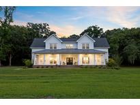 Beautiful two-story white farmhouse with a covered porch, metal roof, and manicured lawn at sunset at 2962 Anchor Watch Dr, Wadmalaw Island, SC 29487