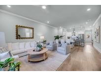 Bright living room with hardwood floors, white sofa and chairs, and open floor plan to kitchen at 7413 Indigo Palms Way, Johns Island, SC 29455