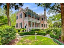 Charming two-story pink home featuring double balconies, a manicured lawn and a lush garden at 62 Eastlake Rd, Mount Pleasant, SC 29464