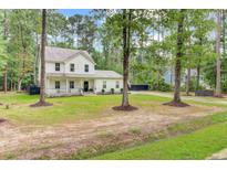 Charming two-story home with a welcoming front porch and lush green lawn surrounded by mature trees at 6190 Button Bush Dr, Ravenel, SC 29470