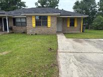 Cozy brick home featuring yellow shutters, a well-maintained lawn, and a paved driveway at 7713 Suzanne Dr, North Charleston, SC 29418