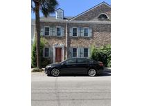 Charming brick townhouse featuring light blue shutters, decorative windows, and a neatly landscaped yard at 128 Queen St, Charleston, SC 29401