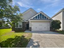 Charming single-Gathering home featuring a two-car garage, stone accents and manicured lawn on a sunny day at 2910 John Cabot Dr, North Charleston, SC 29420