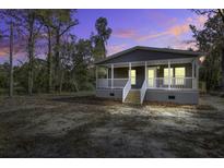 Charming single-story home featuring a covered porch, grey siding, and a well-maintained yard under a vibrant evening sky at 108 Wisteria Falls Ln, Saint Stephen, SC 29479