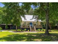 Charming single-story home with a metal roof, inviting porch, and lush, green yard with mature trees at 1515 N Lakeshore Dr, Mount Pleasant, SC 29466