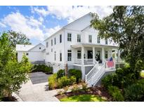 Beautiful two-story white home with an inviting front porch, lush landscaping, and a spacious driveway at 566 Wading Pl, Daniel Island, SC 29492