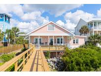Charming pink beach house with a wooden walkway leading to the entrance, nestled among lush greenery at 509 W Ashley Ave, Folly Beach, SC 29439