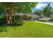 Charming single-story home featuring mature trees, a lush lawn, and a quaint covered front porch with a boat on the driveway at 1098 Blue Marlin Dr, Charleston, SC 29412