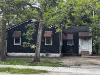 Modest single-story home featuring a black exterior, brick foundation, awning accents and mature trees at 2334 Kent Ave, North Charleston, SC 29405