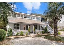 Charming two-story home featuring a welcoming front porch, lush landscaping, and a side staircase to a deck at 504 W Ashley Ave, Folly Beach, SC 29439