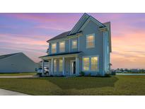 Two-story home with a manicured lawn, covered porch, and traditional architectural details at dusk at 6976 Pumpkinseed Dr, Johns Island, SC 29455