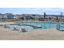 Community pool with in-water lounge chairs and sunbathing deck chairs, and neighborhood homes in the background at 1541 Homecoming Blvd, Ravenel, SC 29470