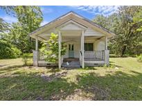 White cottage-style home with a covered front porch and mature trees in the yard, beneath a partly cloudy sky at 1736 Central Ave, Summerville, SC 29483