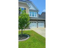 Two car garage with white doors, a stone facade, and a manicured lawn at 322 Braken Fern Rd, Moncks Corner, SC 29461