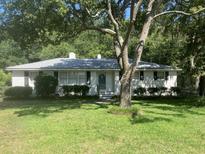 Charming, single-story home with a white brick exterior, a gray roof, and surrounded by lush greenery at 874 Evans Rd, Charleston, SC 29412