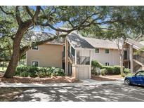 Inviting exterior of a tan condo building with stairs to the second-floor entry under mature tree canopy at 146 High Hammock Villas, Seabrook Island, SC 29455