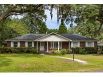 Charming brick home featuring a well-manicured lawn, crisp white shutters and surrounded by mature trees at 1789 Balfoure Dr, Charleston, SC 29407