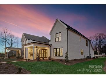 Stunning exterior showcasing a modern white brick home with a covered patio and lush green lawn at dusk at 8163 Fairview Rd, Charlotte, NC 28226
