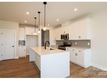 Bright kitchen boasts white cabinets, stainless steel appliances, large island with pendant lighting, and hardwood floors at 133 Armstrong Rd, Belmont, NC 28012
