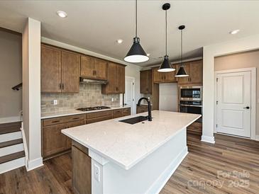 A modern kitchen features a large island with quartz countertops and pendant lighting, complemented by wood-look floors at 139 Armstrong Rd, Belmont, NC 28012