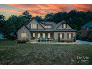 Charming stone and stucco home with a manicured lawn with warm interior lighting at sunset at 7582 Cottonwood Dr # 39, Denver, NC 28037