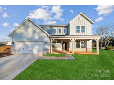 Two-story farmhouse features a front porch, attached two-car garage, and landscaped lawn at 7073 Stella Pl, Stanley, NC 28164