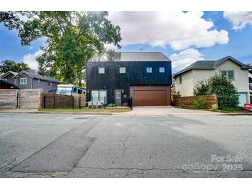 Unique, modern two-story home with a black exterior, beautiful landscaping, and a stained wood garage door at 2107 W Trade St, Charlotte, NC 28216