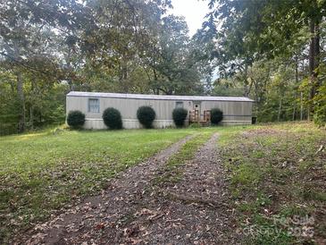 A single-level home featuring a gravel driveway lined with bushes and surrounded by lush trees at 1926 Scenic Dr, Iron Station, NC 28080