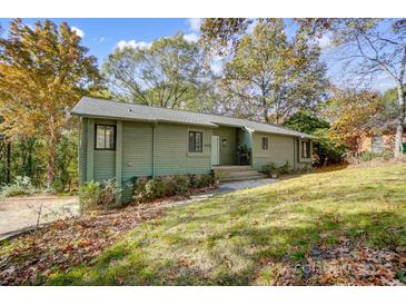 Green siding exterior shot of home in the woods on a sloped lawn in autumn at 11429 Spreading Oak Ln, Charlotte, NC 28226