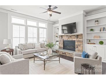 Bright living room featuring a stone fireplace, built-in bookshelves, large windows, and neutral furniture at 1209 Cedar Park Dr, Pineville, NC 28134