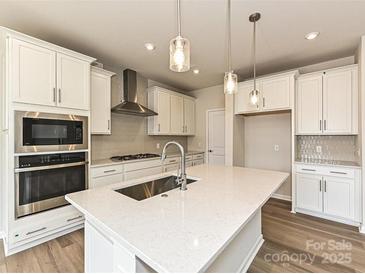 Bright kitchen features stainless appliances, white cabinets, large island and pendant lighting at 8022 Franklin Trail St, Mint Hill, NC 28227