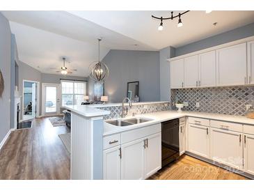 Well-lit kitchen featuring white cabinets, stainless steel sink, breakfast bar and stylish backsplash at 18742 Nautical Dr # 305, Cornelius, NC 28031