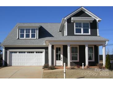 Charming two-story home featuring a white garage door, inviting front porch, and dark siding, perfect for modern living at 13618 Tranquil Day Dr, Matthews, NC 28105