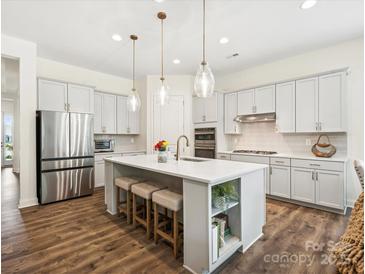 A spacious kitchen features stainless steel appliances, white cabinets, an island with bar stool seating and pendant lighting at 212 Portrait Way, Indian Trail, NC 28079