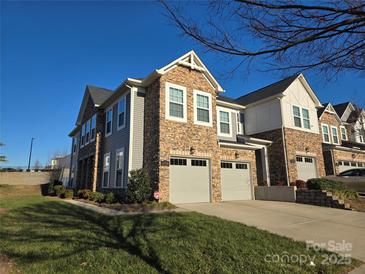 Modern two-story townhome with stone and siding accents, two-car garage, and landscaped lawn at 5860 Clan Maclaine Dr, Charlotte, NC 28278