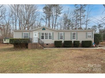 Beige single-wide manufactured home with landscaped lawn and trees at 115 Tradewinds Ct, Mooresville, NC 28115