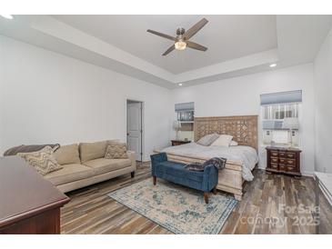 Bright main bedroom featuring a tray ceiling, ceiling fan, sitting area, and decorative rug at 1076 Furnace Rd, Iron Station, NC 28080