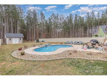 A kidney-shaped pool with a small waterfall feature is surrounded by a stone-paver deck and mature trees at 1076 Furnace Rd, Iron Station, NC 28080