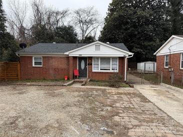 Brick ranch house with a gravel driveway and a wooden fence at 1401 Lasalle St, Charlotte, NC 28216