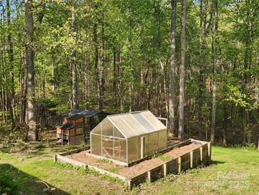 A greenhouse and chicken coop in the backyard surrounded by lush trees and greenery at 888 Brevard Place Rd, Iron Station, NC 28080