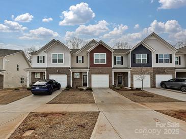 Charming townhome exteriors featuring brick accents and attached garages, set against a blue sky with lovely cloudscape at 14041 Castle Nook Dr # 75, Charlotte, NC 28273