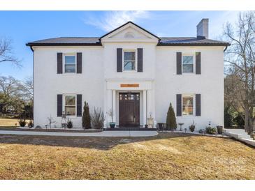 Two-story white brick home with dark metal roof, shutters, and a dark front door at 303 S Greene St, Wadesboro, NC 28170