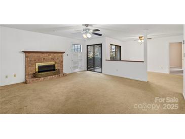 Spacious living room with a brick fireplace, ceiling fan and sliding glass doors to a private patio at 5818 Harris Grove Ln, Charlotte, NC 28212