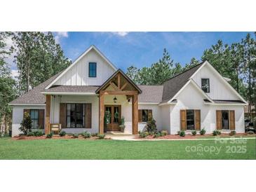 Charming exterior view of a modern farmhouse with white siding, wood accents, and a well-manicured lawn at 295 Tradition Dr, Mount Gilead, NC 27306