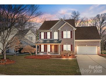 Charming brick two-story home with a well-manicured front yard and a covered porch and two-car garage at 1221 Cochrane Woods Ln, Matthews, NC 28105