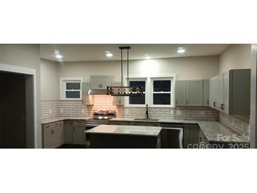 Well-lit kitchen featuring white subway tile backsplash, granite countertops, and gray cabinets at 105 N Inman Ave, Bessemer City, NC 28016