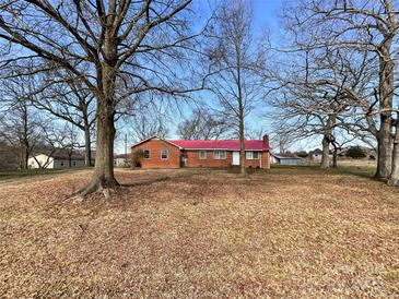 Charming brick home with a bright red roof and a spacious yard surrounded by mature trees on a sunny day at 6523 Prospect Rd, Monroe, NC 28112