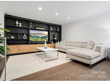 Bright living room featuring a custom built-in shelving unit, hardwood floors, and a comfortable sectional sofa at 7314 Entwhistle Ct, Charlotte, NC 28226