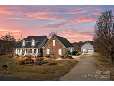 Beautiful brick home with manicured landscaping, long driveway, and detached garage under a gorgeous sunset sky at 144 Cameron Dr, Salisbury, NC 28147